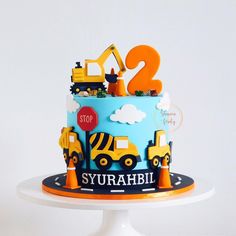 a blue and yellow cake with construction vehicles on it's top is the number two