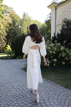 a woman wearing a white dress and heels walking down a cobblestone road with her back to the camera