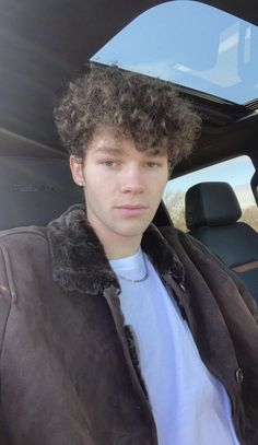 a young man with curly hair sitting in the back seat of a car looking at the camera