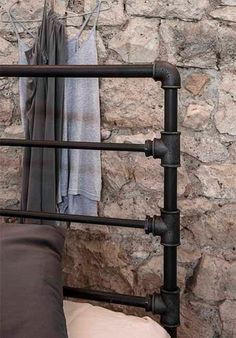 an iron bed frame with two pillows on it and some clothes hanging up against the wall