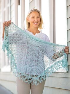 a woman holding up a blue crocheted shawl on the side of a house