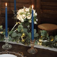 candles are lit on a table with flowers and greenery