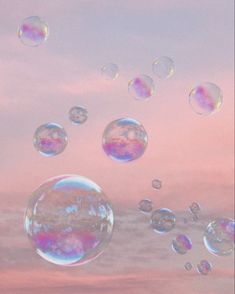 soap bubbles floating in the air on a pink and blue sky with clouds behind them