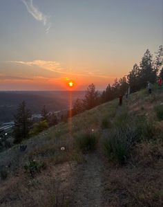 the sun is setting on top of a hill with people walking up and down it