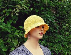 a mannequin head wearing a yellow crochet hat in front of trees