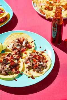 three tacos are sitting on a blue plate next to a bottle of beer and some tortillas