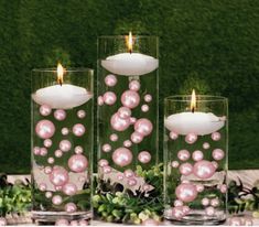 three glass vases filled with pink pearls and candles sitting on a table next to greenery