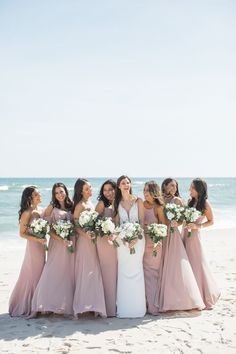 a group of women standing next to each other on top of a sandy beach near the ocean