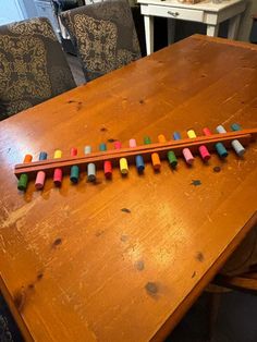 a wooden table with colored crayons on it and two chairs in the background