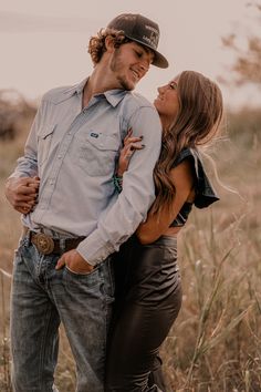 a man and woman embracing in the middle of a field with tall grass behind them