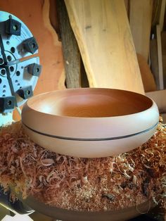 a wooden bowl sitting on top of a pile of wood shavings next to a machine