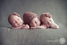 three newborn babies are sleeping together on a gray couch with their heads turned to the side