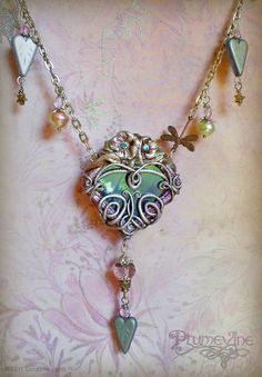 a necklace with an ornate heart and charms hanging from it's sides on a pink background