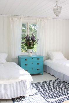 two beds in a room with white walls and blue dresser next to eachother