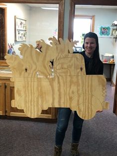 a woman holding up a cut out of a wooden horse in front of a mirror