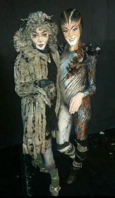 two people dressed in costumes standing next to each other on a black surface with dark background