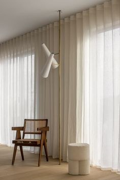 a wooden chair sitting next to a tall lamp in a room with white drapes on the windows