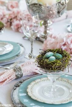 the table is set with plates, silverware and small bird's nests