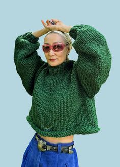 an older woman wearing sunglasses and a green sweater is holding her hands up to her head