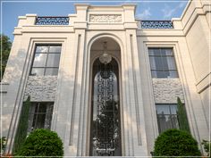 a large white building with a clock on it's face and bushes in front