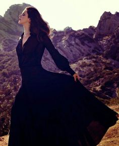 a woman in a long black dress standing on top of a mountain