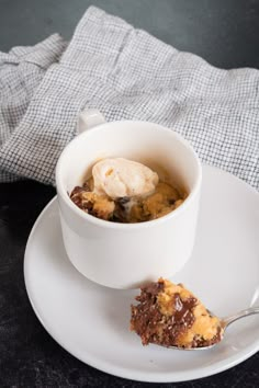 a white plate topped with a piece of cake next to a cup of ice cream