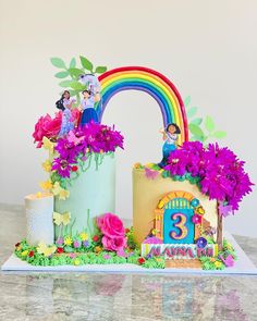 a birthday cake decorated with flowers and characters on the top is an arch shaped like a rainbow