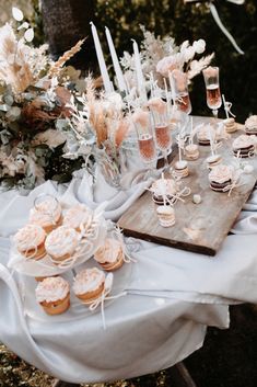 a table topped with cupcakes and desserts on top of a white cloth