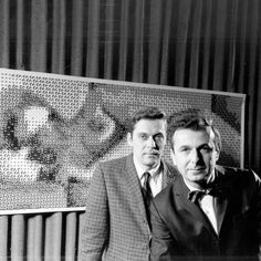 two men standing next to each other in front of a painting