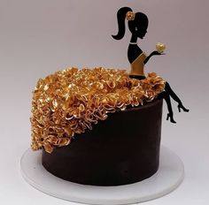 a cake decorated with gold ruffles and a woman sitting on top of it