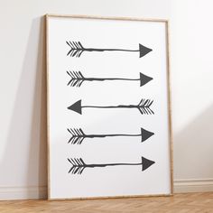 an art print with black arrows on it in front of a white wall and wooden floor