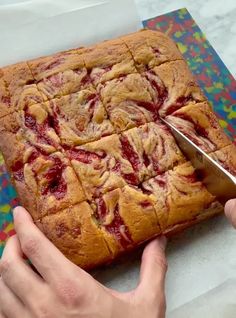 a person cutting into a square cake with a pair of scissors on top of it