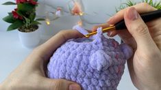 someone is crocheting a small purple object with a yellow knitting needle in their hands