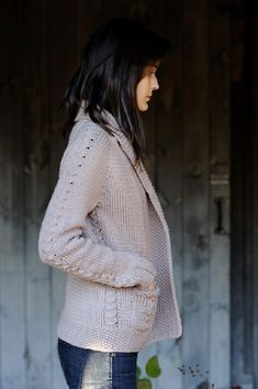 a woman standing in front of a wooden door wearing jeans and a sweater with holes on it