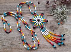 a multicolored beaded necklace on a wooden table next to some dried flowers