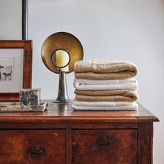 a wooden dresser topped with lots of folded towels and a light on top of it