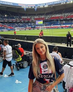 a beautiful young woman standing in front of a soccer stadium filled with fans and spectators