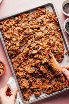 two hands holding a wooden spoon over a baking pan filled with granola