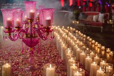 a pink chandelier surrounded by candles and rose petals on the ground at a wedding