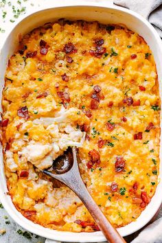 a casserole dish with chicken, cheese and bacon in it next to a wooden spoon