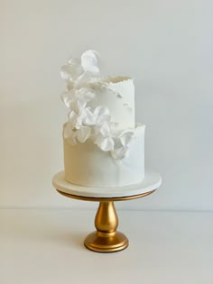 there is a white cake with flowers on the top and gold base, sitting on a table