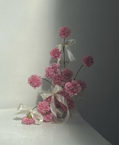 pink carnations and white ribbons are arranged in a vase on a countertop