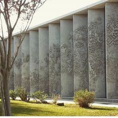 a concrete wall with carvings on it next to a tree and bushes in the foreground