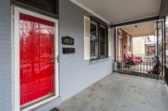 a red door sits on the front porch of a house with white brick walls and black iron railings