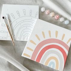 two small paintings on top of a bed next to a pen and thread spools