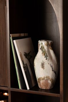 a white vase sitting on top of a wooden shelf next to an open bookcase