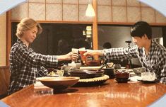 two people sitting at a table with food in front of them and one person reaching for something