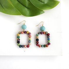 Tiny, colorful Kantha beads form a square and dangle from a larger center bead to create a geometric statement earring. Bohemian Square Multicolor Jewelry, Bohemian Rectangular Ear Wire Earrings, Bohemian Rectangular Earrings With Ear Wire, Bohemian Multicolor Rectangular Earrings, Bohemian Multicolor Rectangular Jewelry, Handmade Multicolor Rectangular Beaded Earrings, Multicolor Rectangular Beaded Earrings As Gift, Nickel-free Multicolor Rectangular Earrings, Bohemian Rectangular Beaded Earrings With Ear Wire