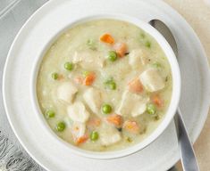 a bowl of chicken and dumpling soup on a plate with a spoon next to it