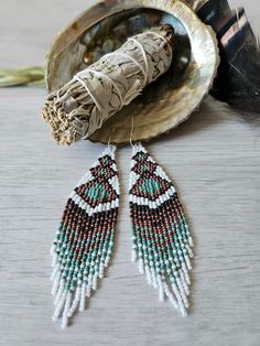 a pair of beaded earrings sitting on top of a shell next to a feather